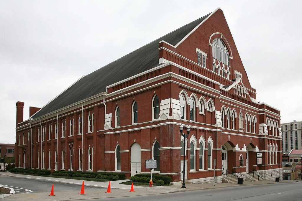 Historic red-brick building with arched windows and a peaked roof, located on a city street.